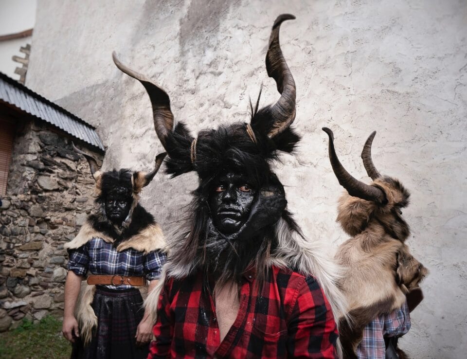 three people standing next to a building wearing costumes made from sheep horns and wool